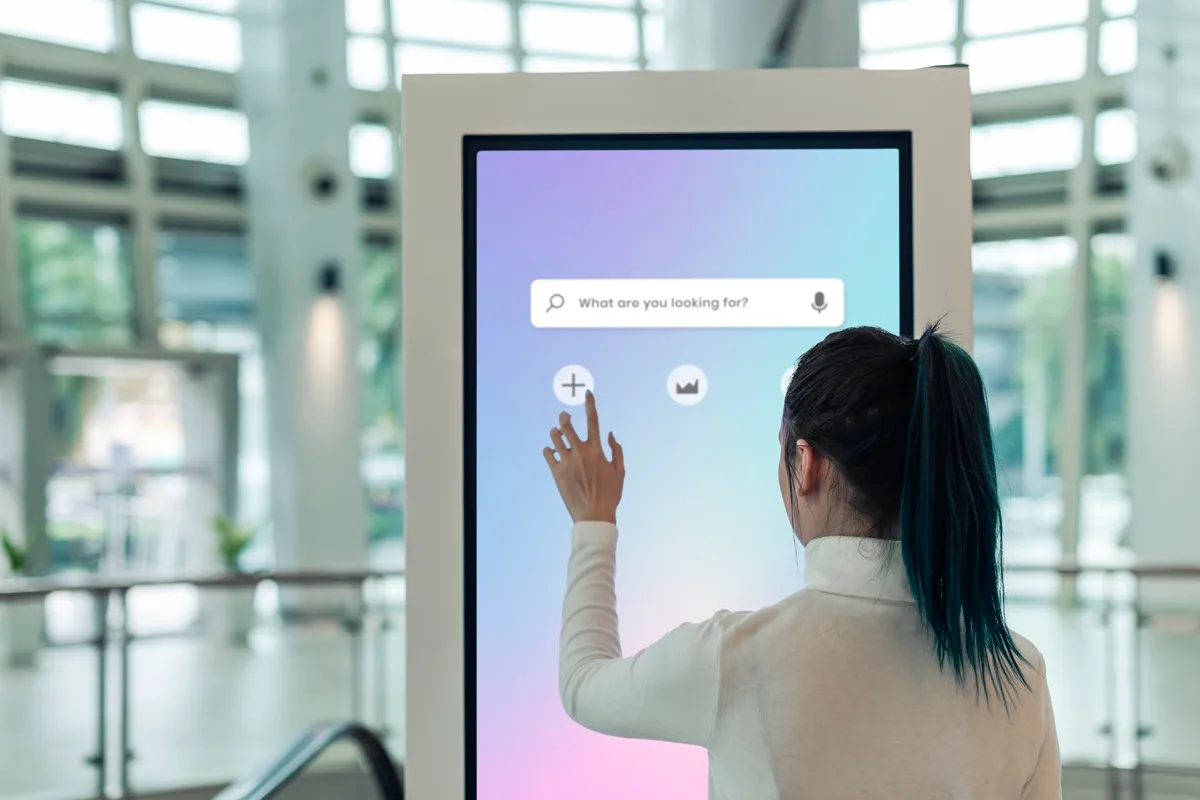 Mulher de costas usando quiosque touchscreen grande com barra de pesquisa em saguão moderno