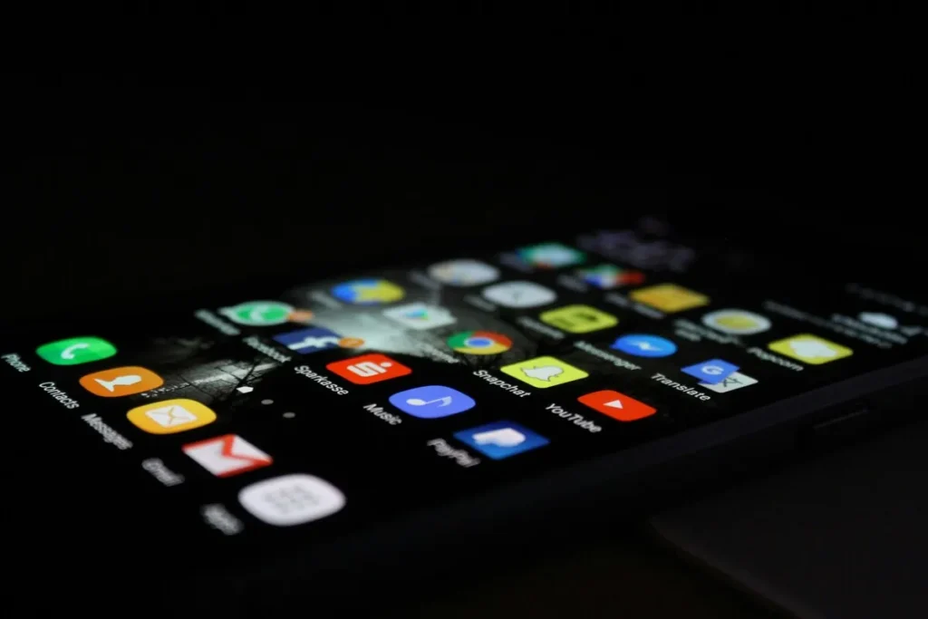 Tela de smartphone exibindo uma variedade de ícones de aplicativos coloridos em um ambiente escuro, representando a diversidade de funcionalidades digitais disponíveis.