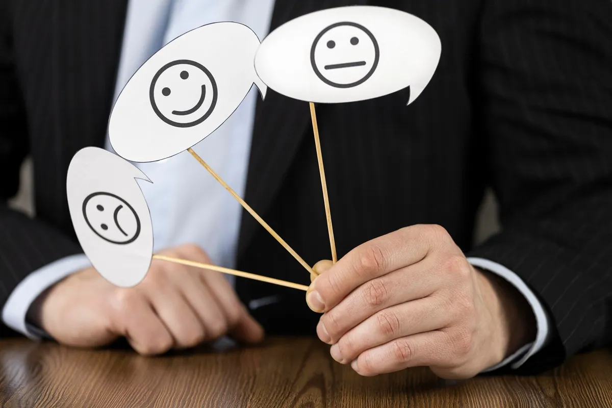 Homem de terno segura três plaquinhas em formato de balão de fala com emojis de satisfação: um sorridente, um neutro e um triste, simbolizando níveis de feedback de cliente