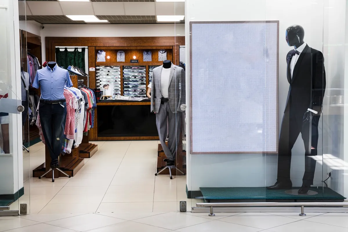 Vitrine de loja de roupas masculinas em shopping center com manequins exibindo ternos, camisas e acessórios