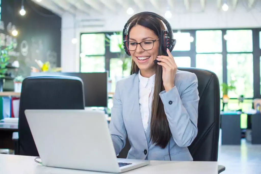 Operadora amigável de suporte ao cliente usando laptop no escritório, utilizando dicas de excelência em atendimento.