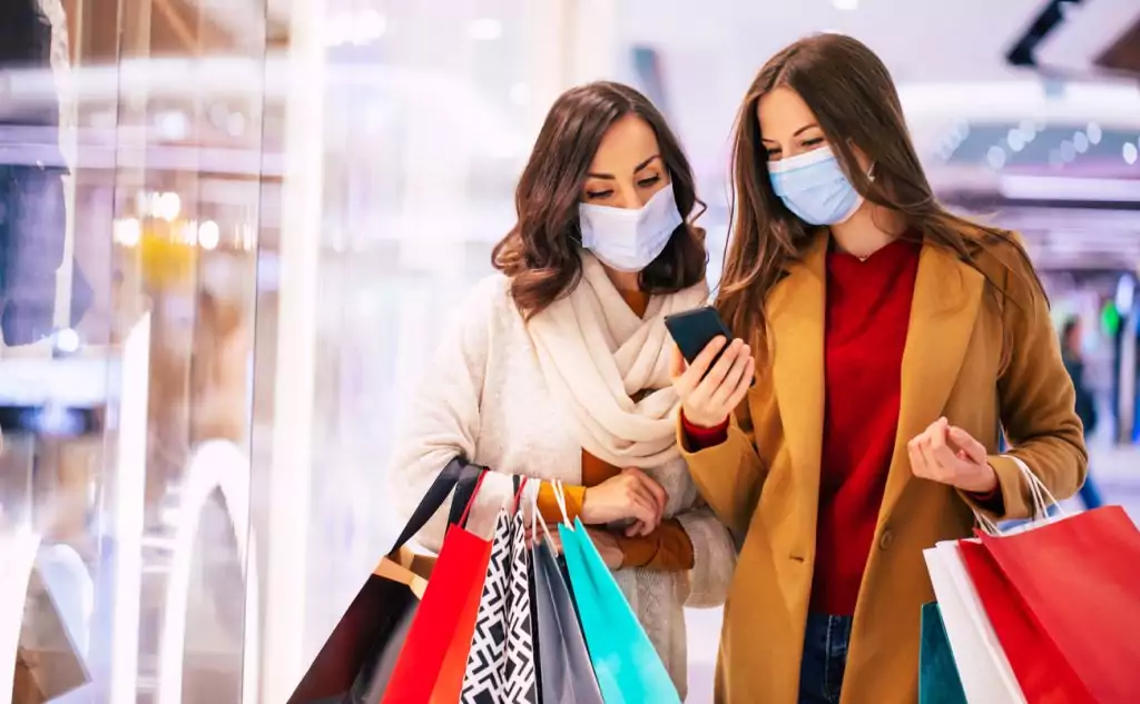 Duas jovens amigas com máscaras médicas de segurança durante compras no shopping, conhecendo as tendências no varejo em 2022