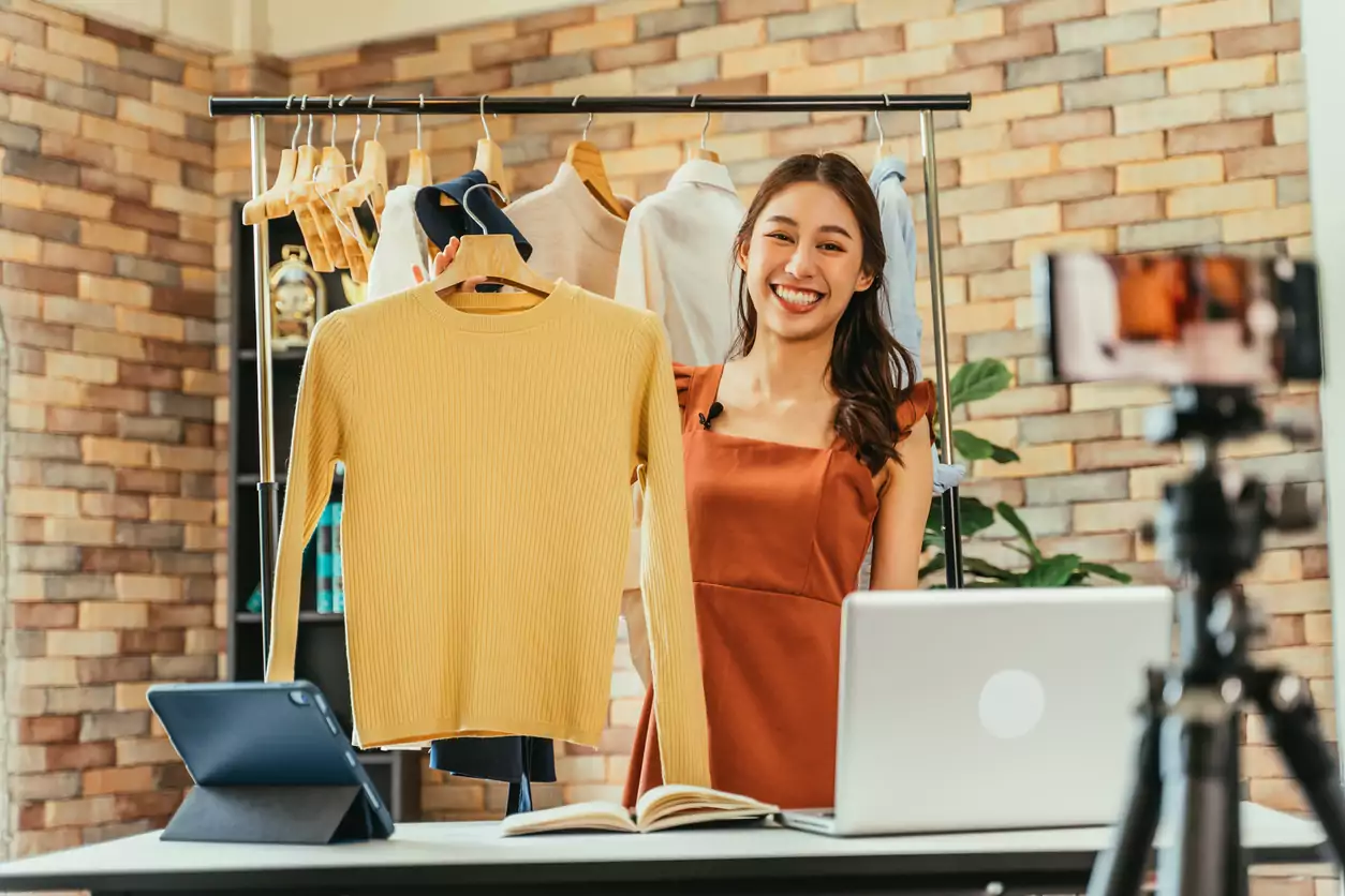 Mulher influenciadora vendendo roupas online em uma live commerce.