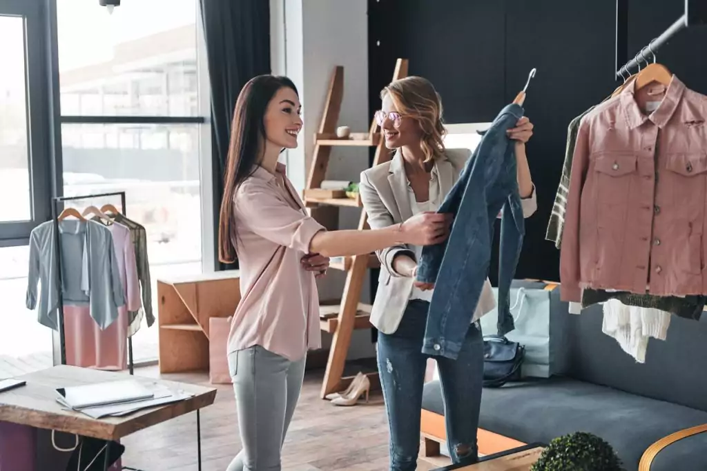 Mulher jovem e bonita ajudando a escolher roupas para seu cliente enquanto trabalhava na boutique de moda. Melhores práticas de varejo sem atrito.