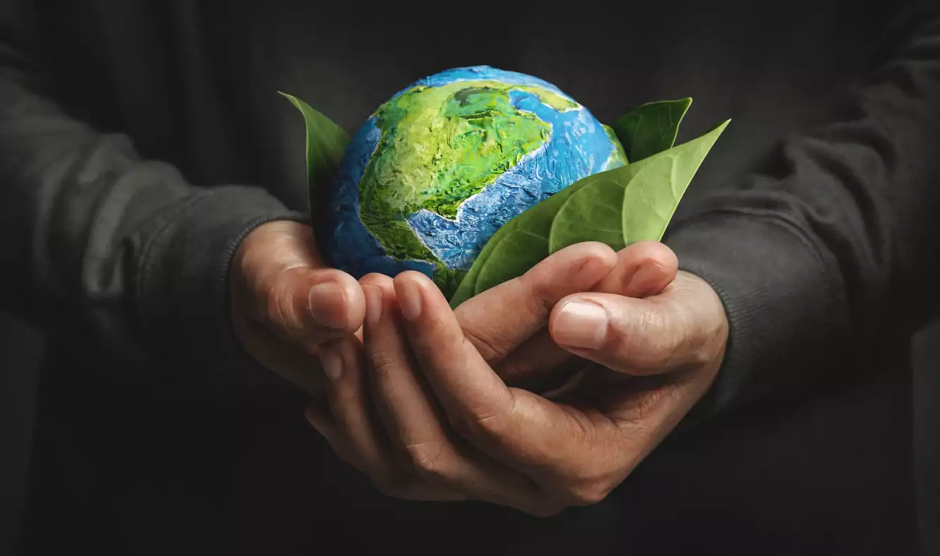 Um homem está segurando o planeta Terra, que está envolto em folhas de árvore. O planeta está saudável graças ás técnicas de Economia Circular
