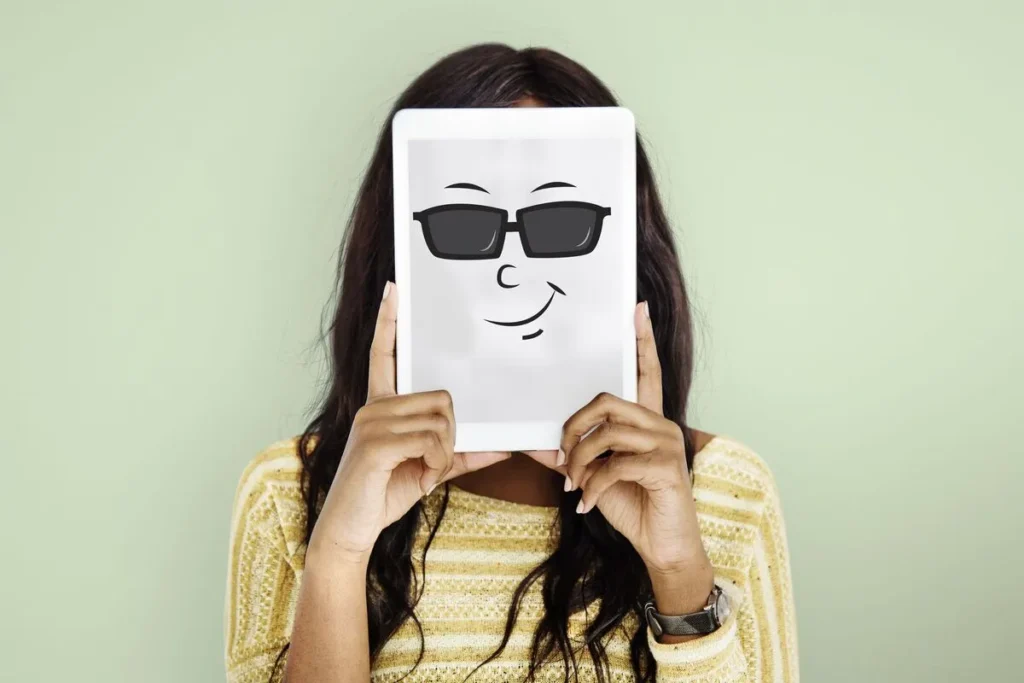 Uma mulher segurando um tablet à frente do rosto. Na tela do tablet, há uma ilustração de um rosto sorridente com óculos escuros, simbolizando um cliente oculto.