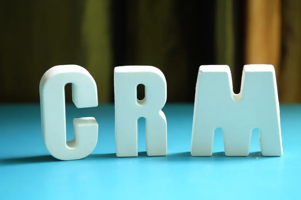 Letras tridimensionais formando a sigla CRM sobre uma mesa azul, com fundo desfocado.