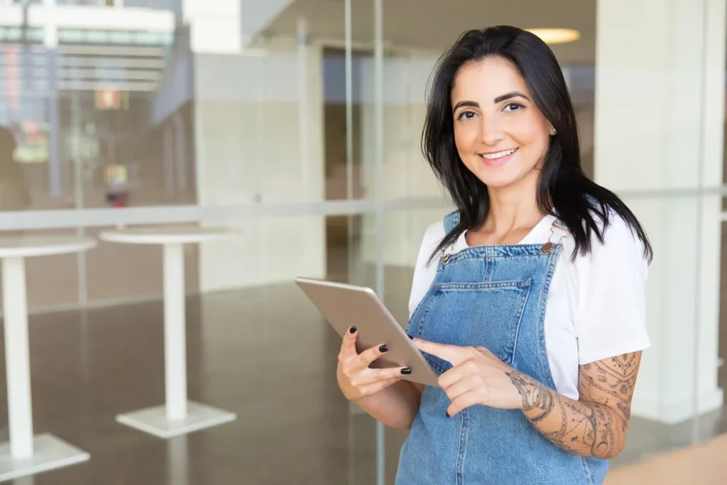 Mulher sorridente segurando um tablet em um ambiente corporativo, representando a importância das avaliações empresariais.