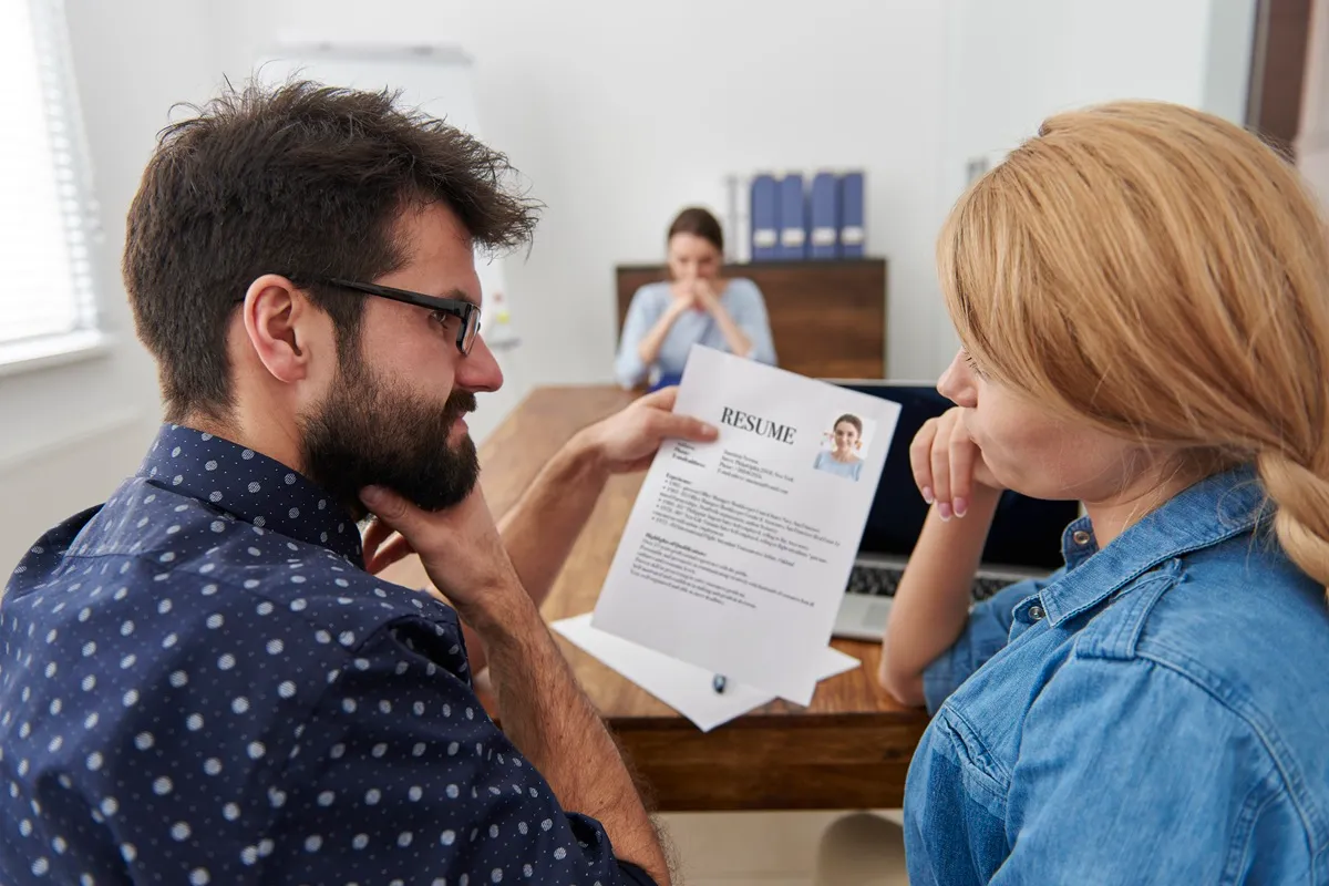 Dois recrutadores analisando um currículo durante uma entrevista de emprego em um escritório moderno.