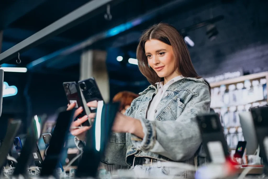 Jovem mulher experimentando smartphones em uma loja de eletrônicos, analisando a câmera e os recursos dos dispositivos.