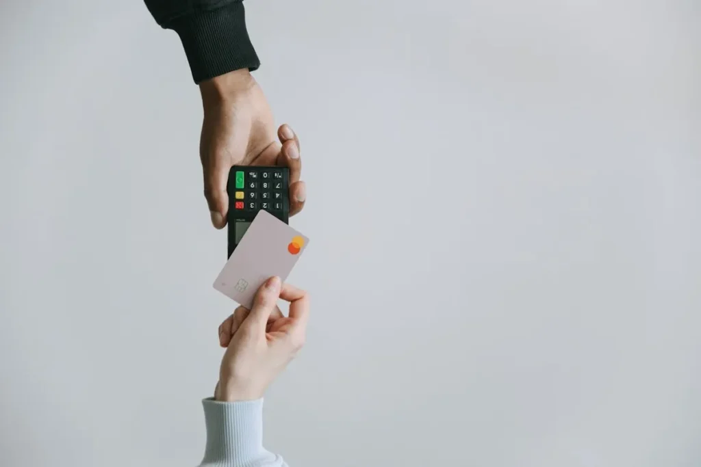 Duas mãos, uma segurando um terminal de pagamento e a outra um cartão de crédito. A imagem simboliza uma transação e a sua relevância para o Customer Lifetime Value (CLV).