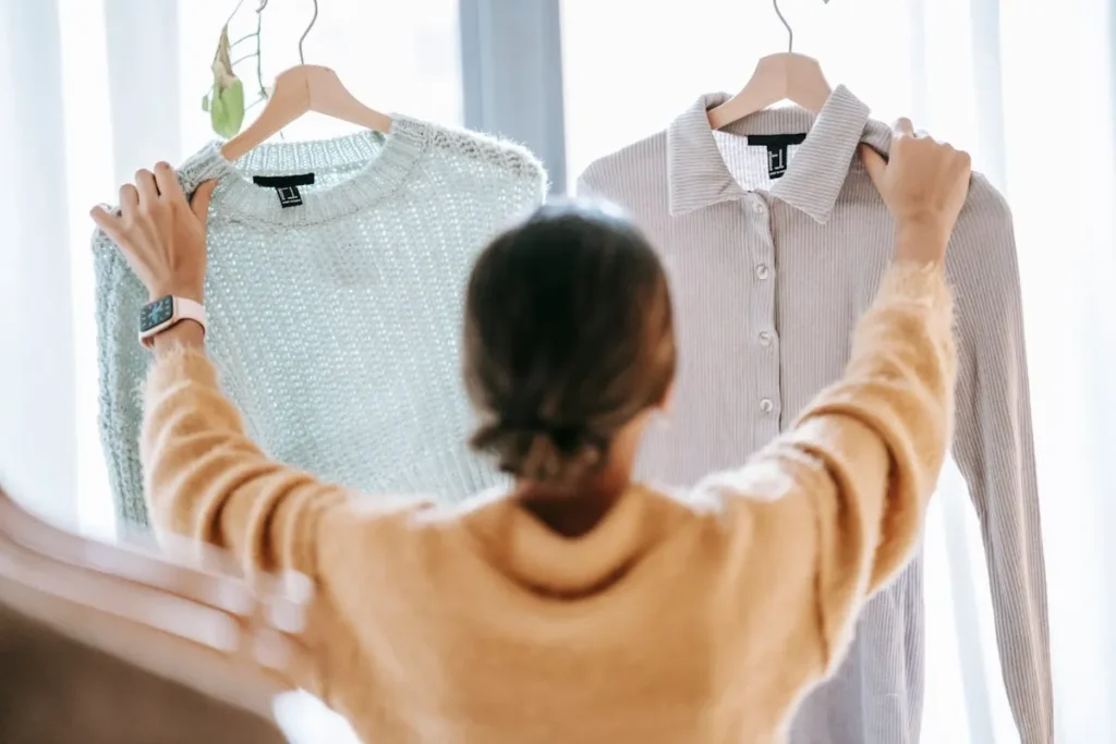 Uma pessoa, vista de costas, a segurar dois cabides com peças de roupa — uma camisola e uma camisa — a representar a escolha do cliente e a construção do Customer Lifetime Value (CLV).