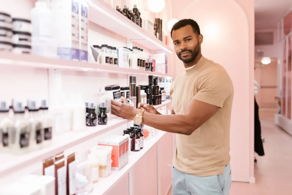 Um homem em uma loja de produtos de beleza, a olhar para a câmara enquanto pega um produto numa prateleira rosa. A imagem representa a jornada do cliente e a construção de um relacionamento a longo prazo, essencial para o CLV.