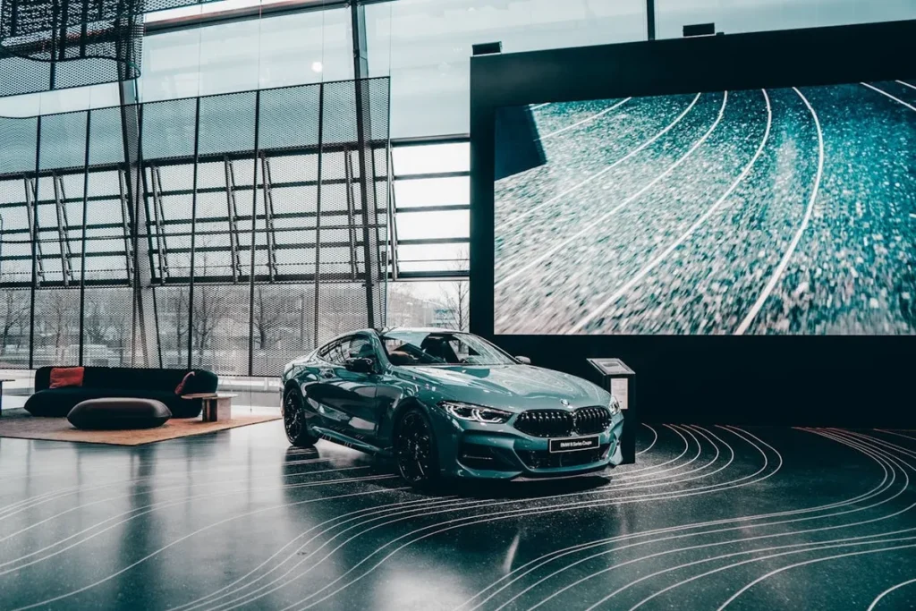 Interior de uma das modernas concessionárias da BMW, exibindo um carro cupê esportivo e uma tela digital gigante.