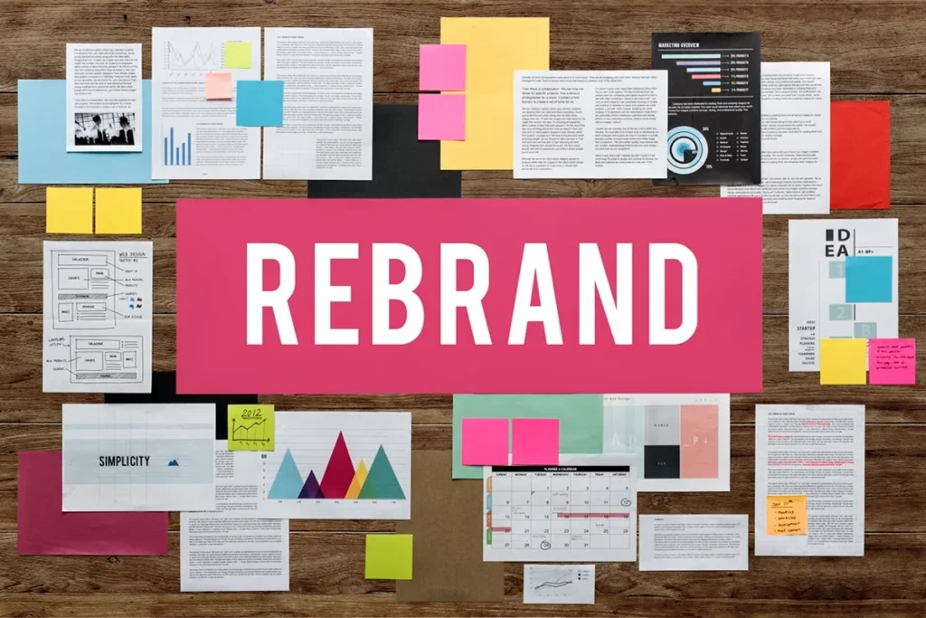 Painel estratégico de rebranding com documentos, gráficos e anotações organizados em uma mesa de madeira, destacando a palavra "REBRAND" no centro.
