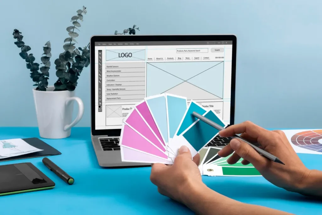 Mãos segurando um leque de amostras de cores em frente a um notebook com um design de site, representando o processo de criação de uma nova identidade visual ou rebranding.