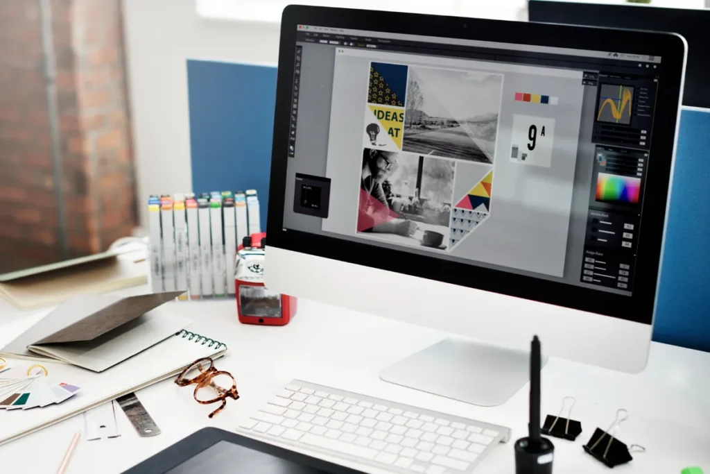 Uma mesa de trabalho de design com um monitor mostrando um projeto de design gráfico, representando o processo de rebranding de uma marca.