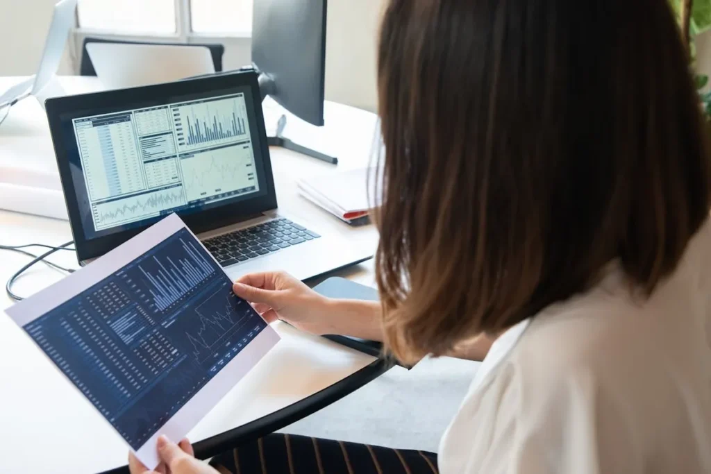 Mulher de negócios analisando gráficos em um laptop e folha impressa, simbolizando o turismo de dados.
