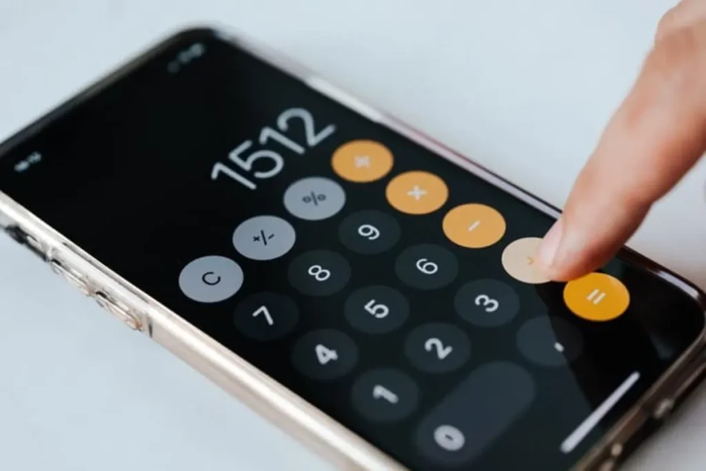 Uma mão pressiona o botão de uma calculadora em um smartphone, ilustrando o cálculo de markup e o uso de ferramentas digitais para finanças.