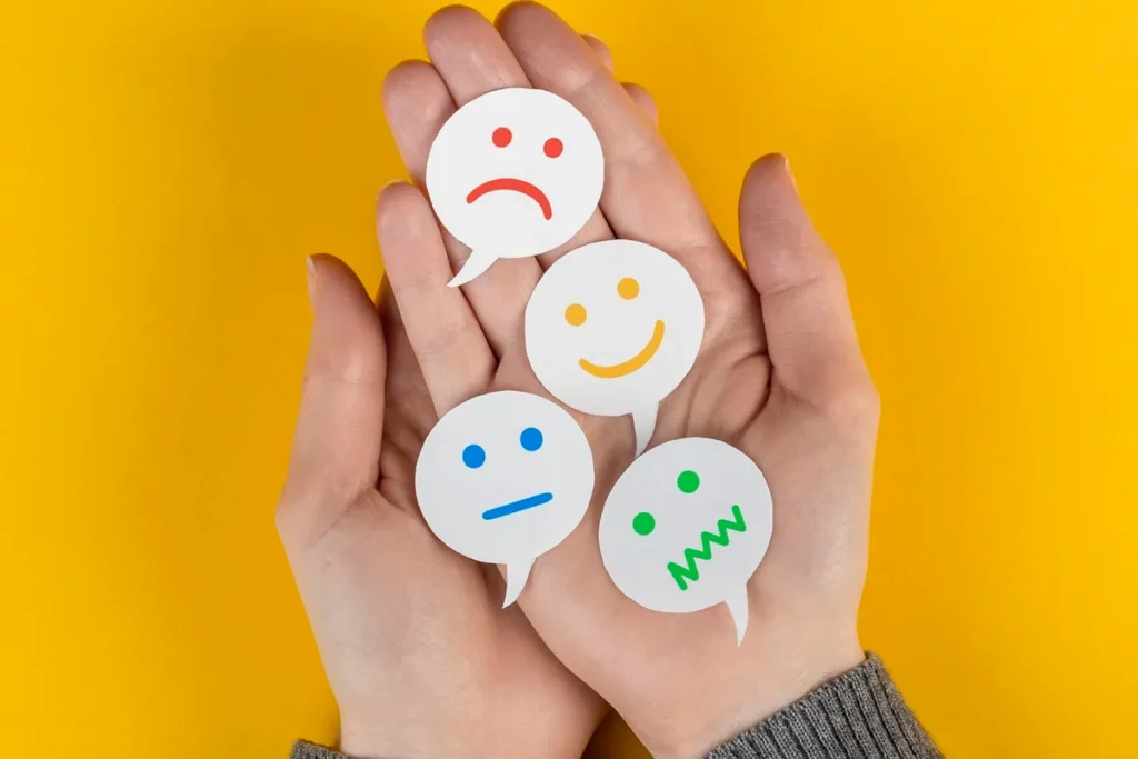 Mãos segurando recortes de balões de fala com rostos expressando diferentes emoções, simbolizando avaliação de satisfação do cliente.