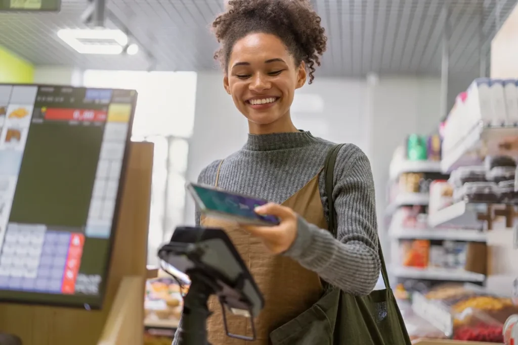 Mulher sorridente segurando cartão ou celular faz pagamento em caixa de autosserviço em supermercado moderno