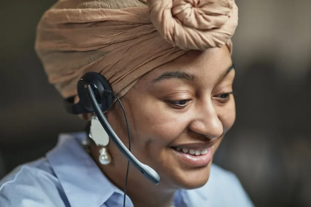 Close-up de uma consultora de vendas com um sorriso simpático, a usar um headset e um turbante, a representar um atendimento ao cliente profissional e acessível.