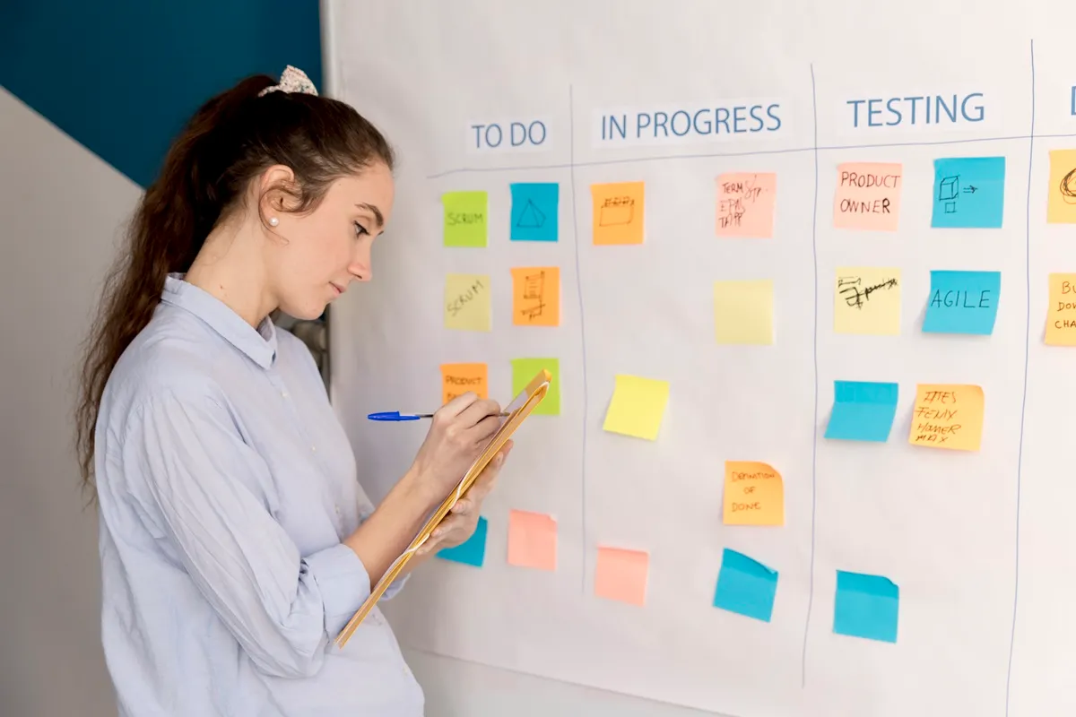 Mulher analisando quadro Kanban com post-its organizados nas etapas To Do, In Progress e Testing.