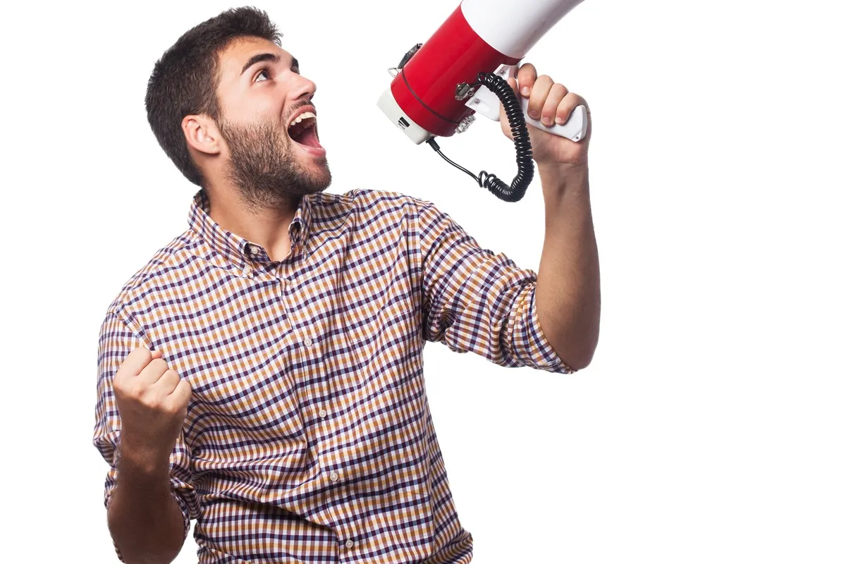 Homem jovem com camisa xadrez segurando um megafone vermelho e comemorando com expressão animada