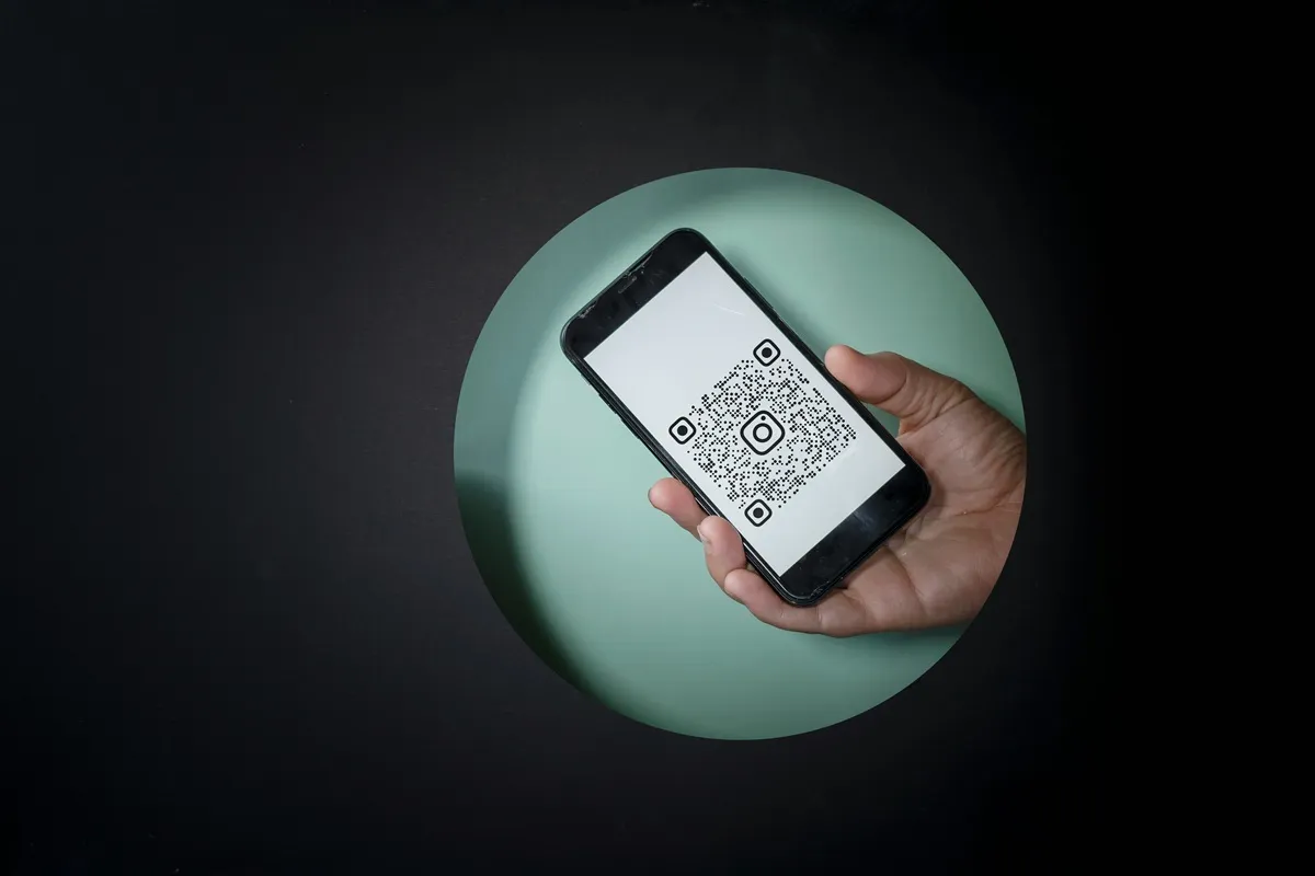 Pessoa segurando celular com QR Code do Instagram na tela, em fundo escuro com círculo verde centralizado, simbolizando acesso rápido ao perfil.