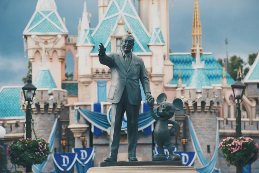 Estátua de Walt Disney de mãos dadas com o Mickey Mouse em frente ao castelo da Disneyland, símbolo da excelência em experiência do cliente.