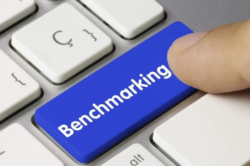 Dedo pressionando a tecla azul com a palavra "Benchmarking" em um teclado de computador.