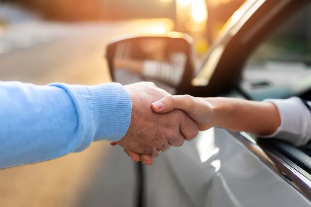 Pessoa apertando as mãos de um atendente em um drive-thru de carro, com luz suave ao fundo