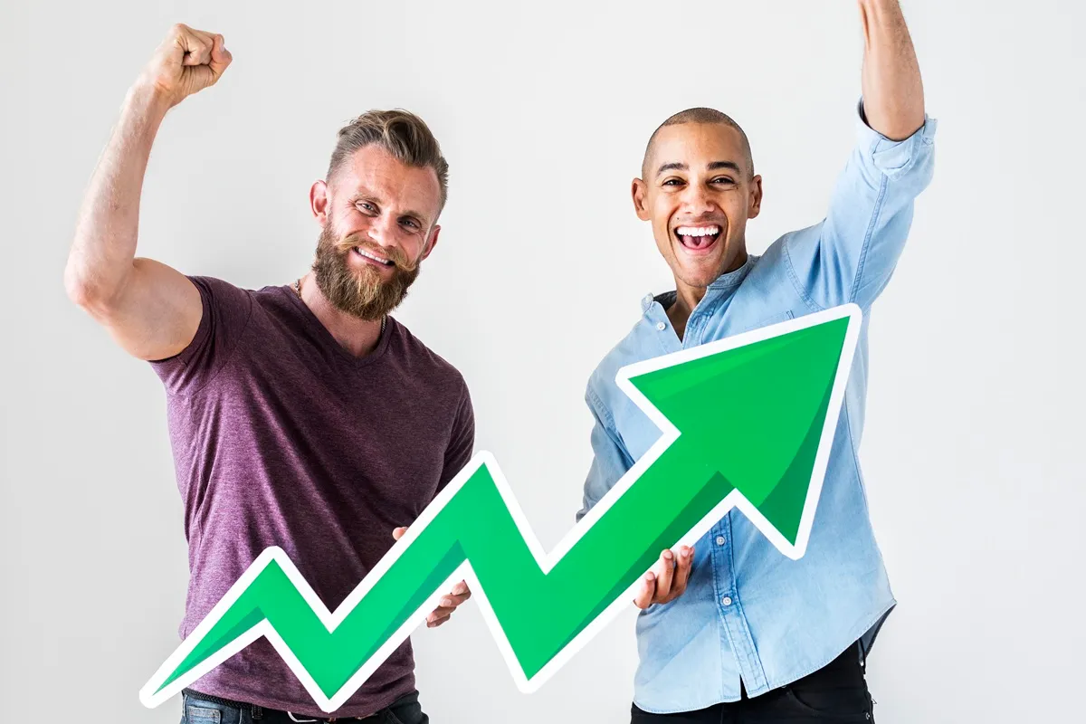 Dois homens sorridentes comemorando o sucesso, com um gráfico de crescimento verde acima deles, simbolizando progresso financeiro ou profissional. Um homem usa uma camiseta roxa e o outro uma camisa azul claro.