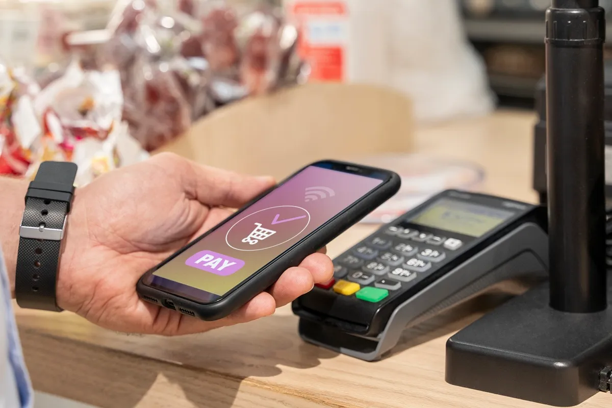 Pessoa realizando pagamento por smartphone via tecnologia NFC em terminal de ponto de venda (POS).