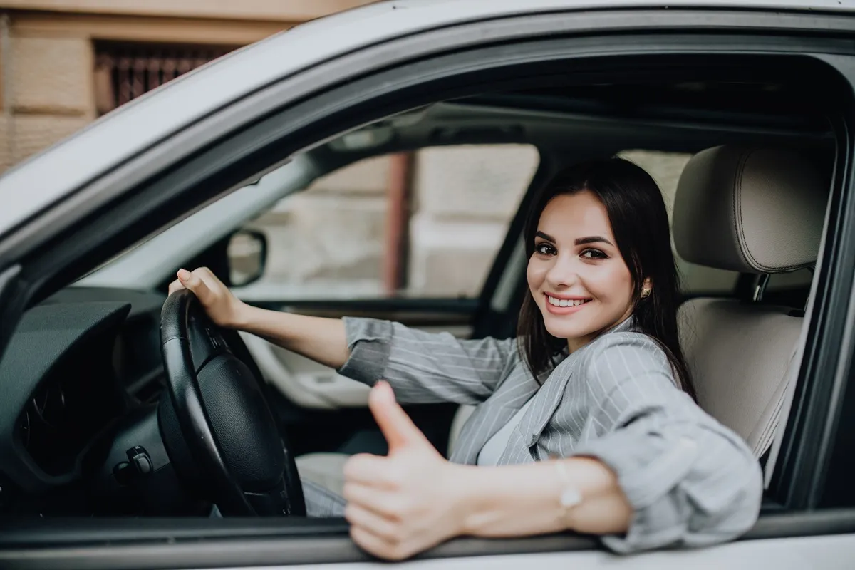 Mulher sorridente em carro fazendo sinal de positivo com a mão em um drive-thru