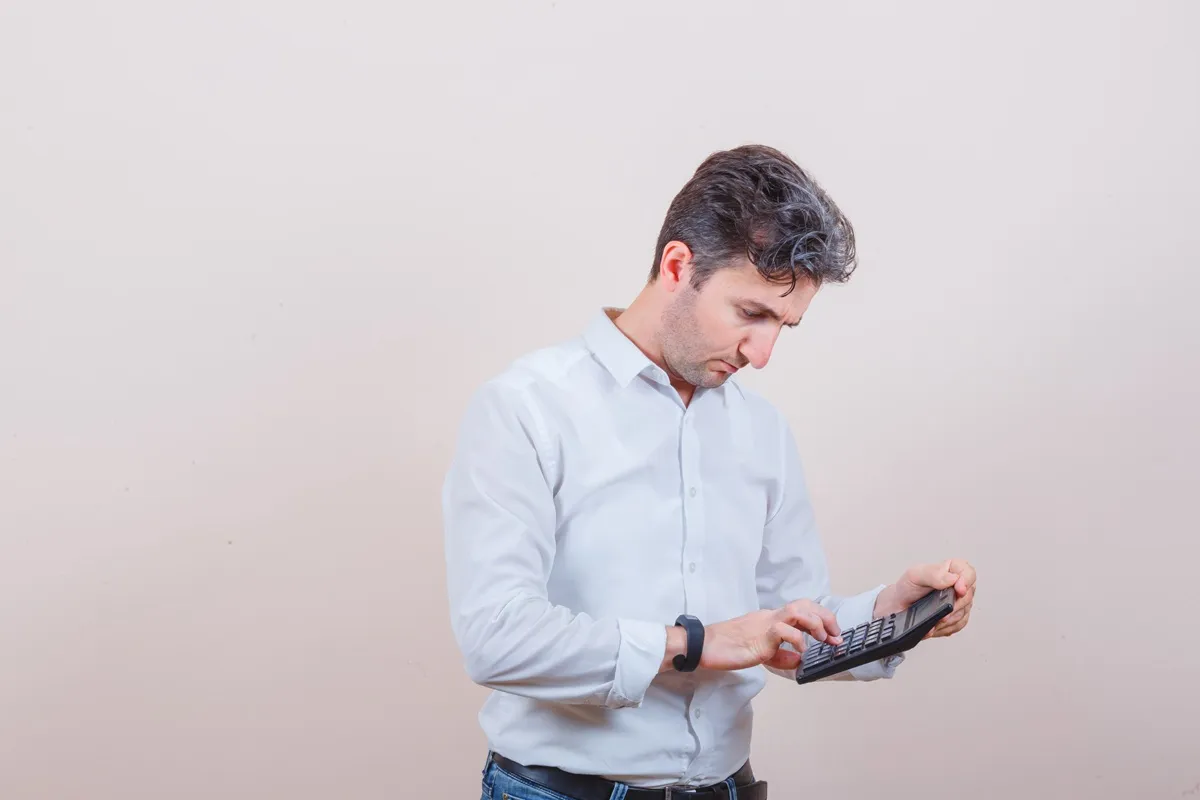Imagem de um homem em um escritório, concentrado, utilizando uma calculadora para realizar cálculos financeiros.