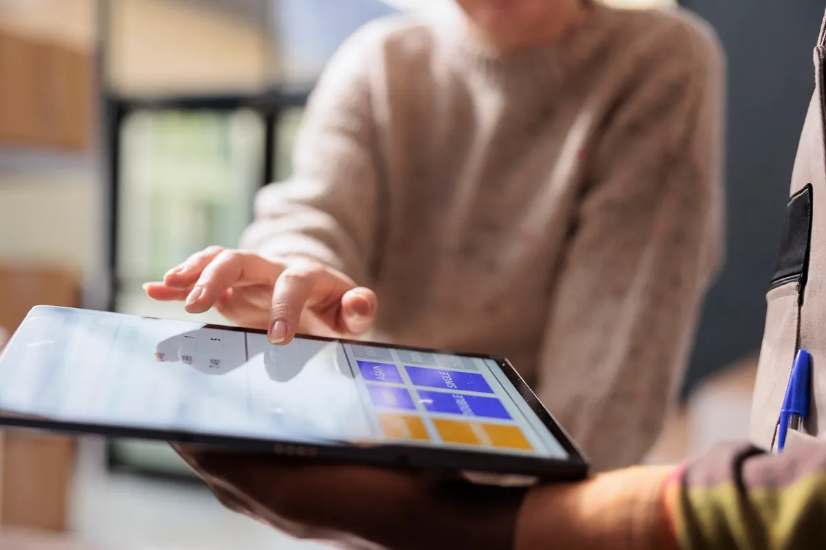 Pessoa usando o dedo para interagir com aplicativo em tablet, visualizando ícones coloridos de categorias como vendas, negócios e mais. A interface exibe gráficos e opções de navegação