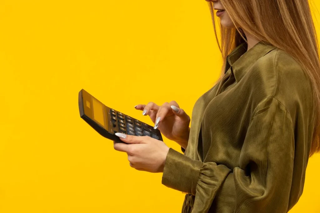 Imagem de uma mulher digitando em uma calculadora, com fundo amarelo vibrante, simbolizando o cálculo de finanças e payback.
