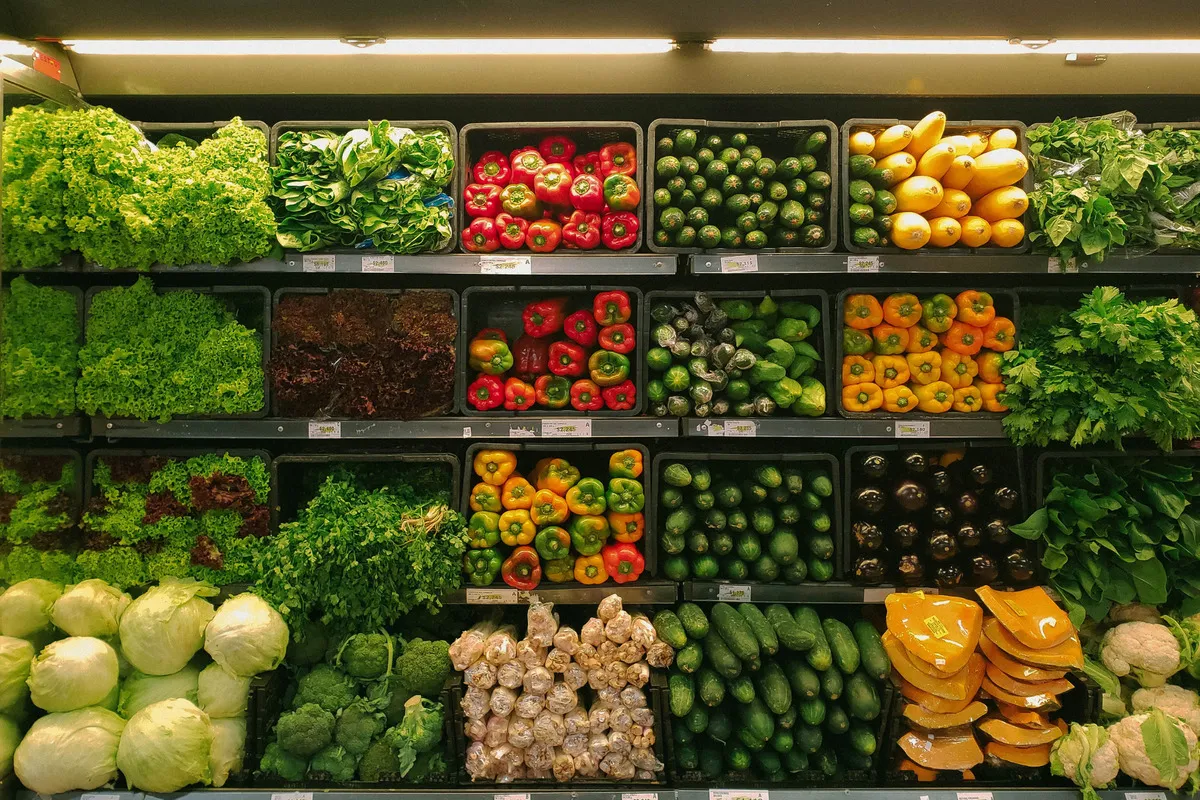Prateleira de supermercado com um planograma de frutas e vegetais frescos. O layout mostra caixas organizadas com alface, pimentões coloridos, abobrinhas e outros itens.