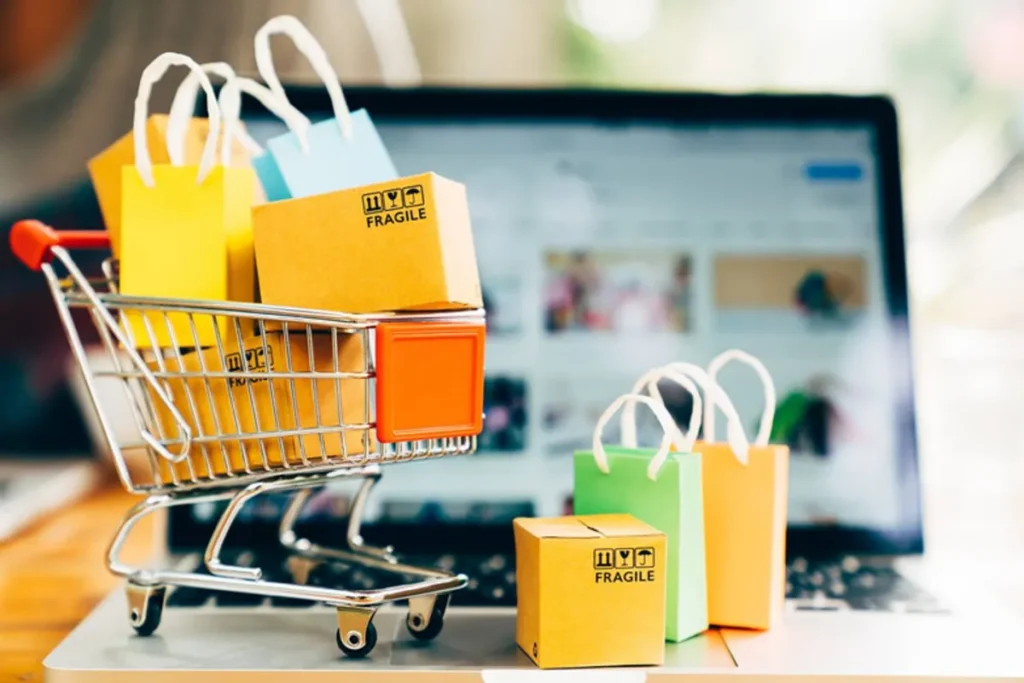 Miniatura de carrinho de compras de supermercado com caixas e sacolas coloridas sobre teclado de laptop, representando e-commerce, vendas online e estratégias de trade marketing digital.