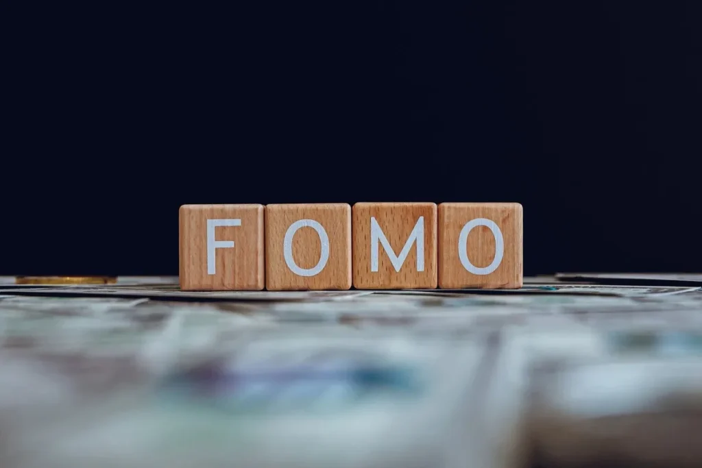 Blocos de madeira com a palavra FOMO sobre superfície com dinheiro ao fundo escuro