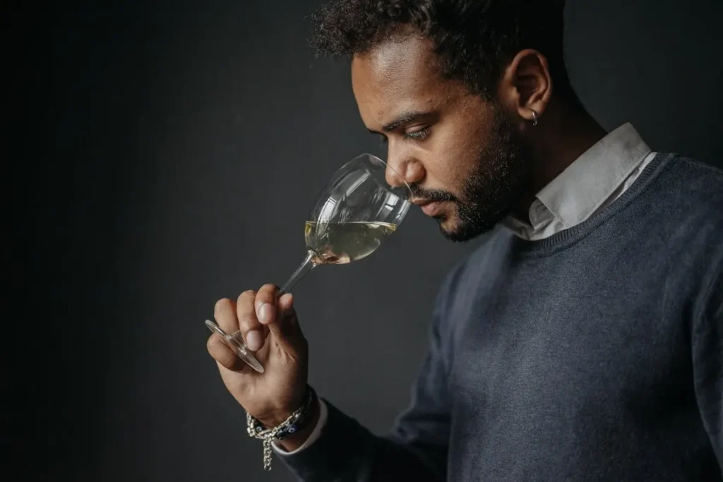 Homem cheirando taça de vinho branco, representando o sentido do olfato.
