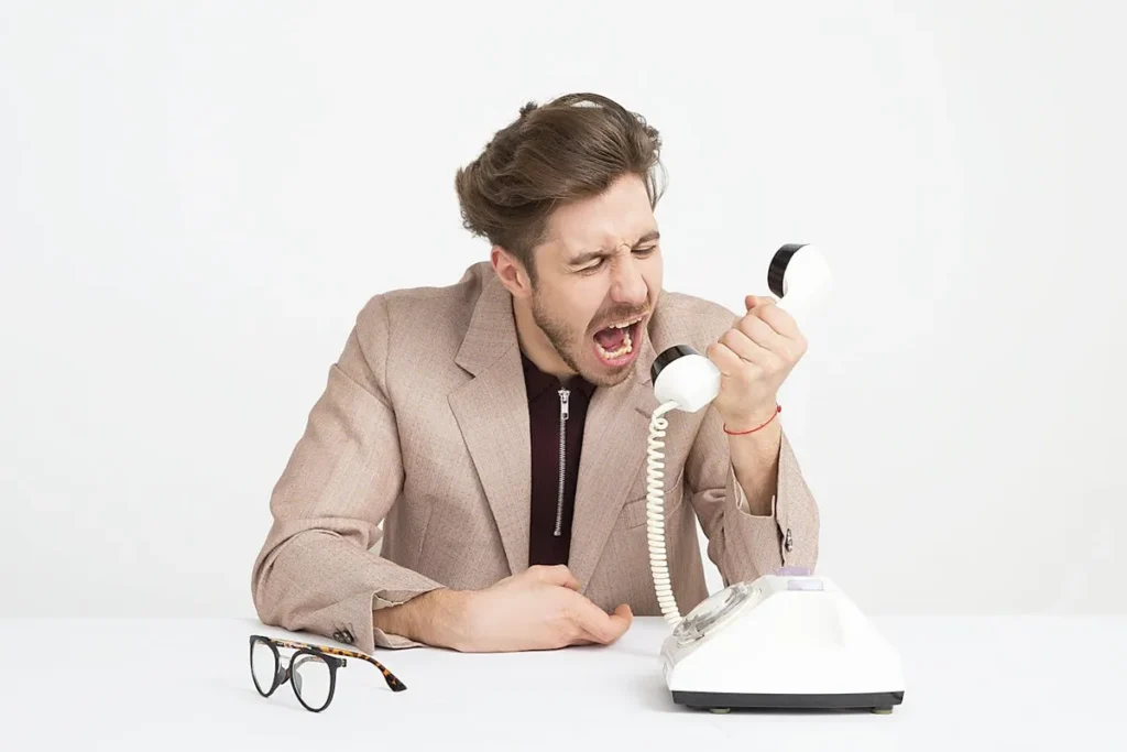Homem irritado gritando ao telefone, representando um cliente detrator insatisfeito.