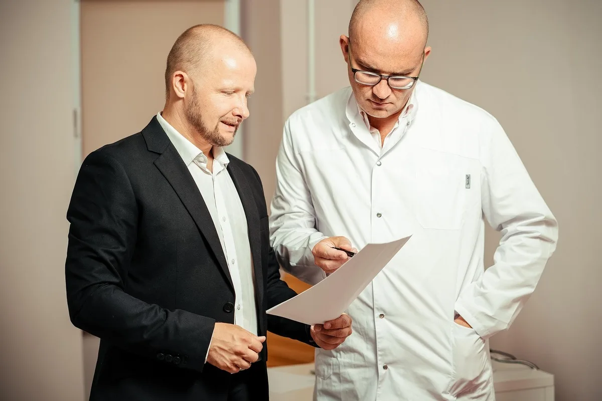 Empresário e médico analisando documento em consultório.