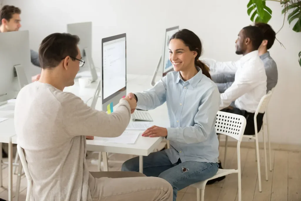 Dois colegas de trabalho sorridentes, representando consistência e colaboração, apertam as mãos em um escritório.