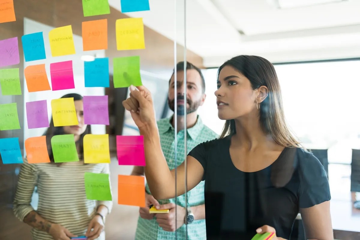 Equipe de três pessoas discutindo ideias de endomarketing em frente a um vidro cheio de post-its coloridos