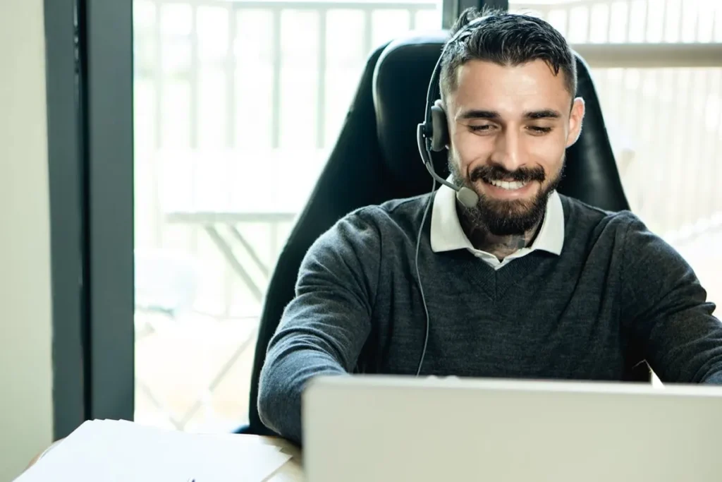 Homem sorrindo com headset e laptop, representando suporte ao cliente e aprimoramento da experiência do cliente.