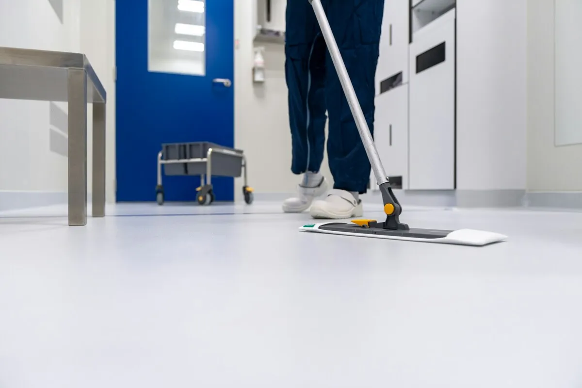 Profissional de limpeza higienizando o chão com esfregão em ambiente hospitalar.