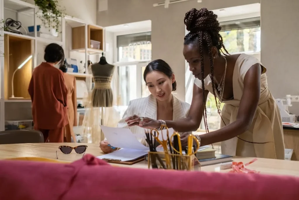 Duas mulheres discutem projeto de moda em ateliê com manequins ao fundo
