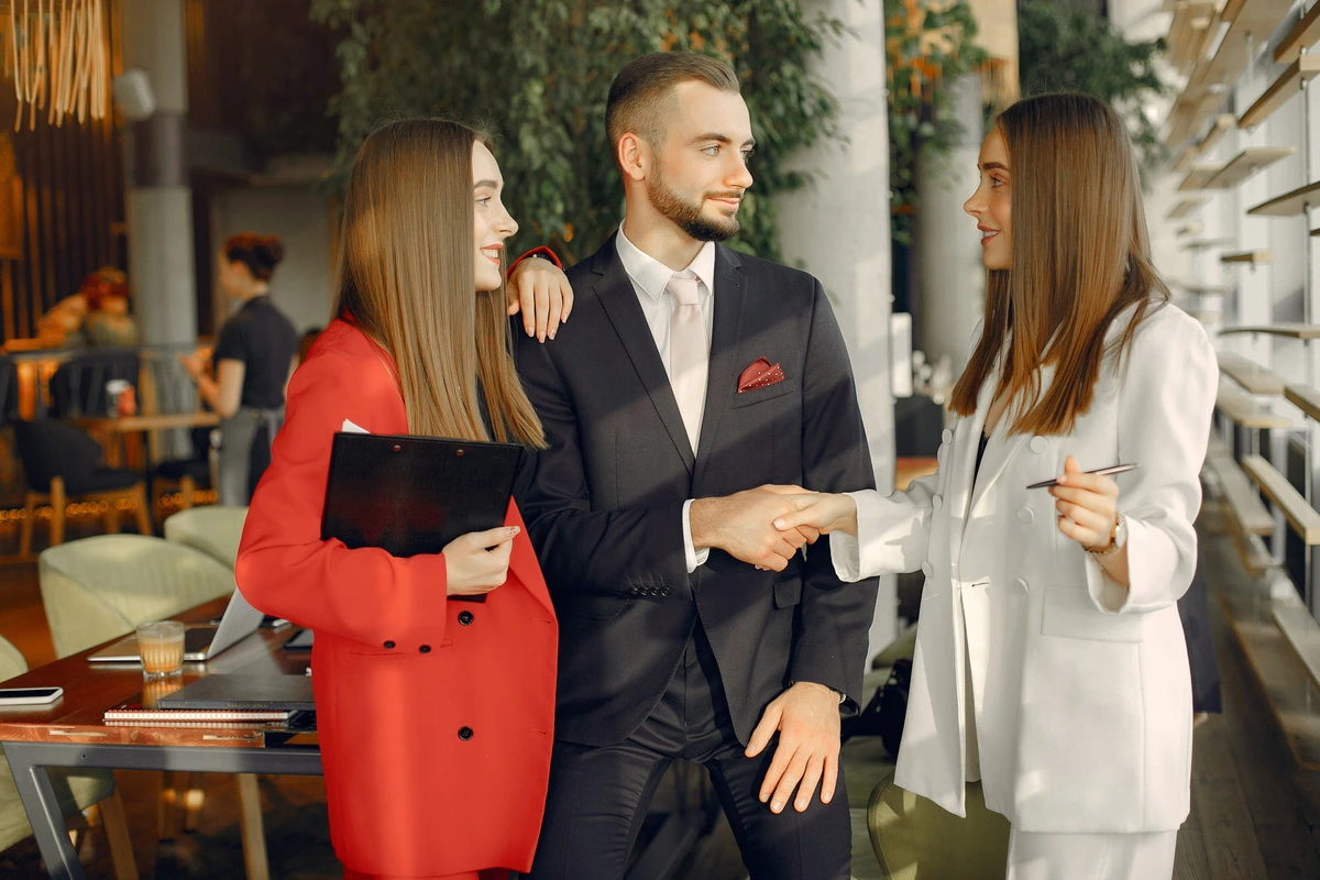 Três profissionais bem-vestidos cumprimentando-se em ambiente corporativo moderno.